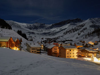 Houses by snowcapped mountains against sky at dusk