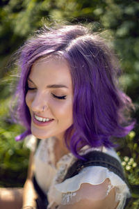 Portrait of a teenage girl with purple hair and an earring in her nose sit in the grass in nature