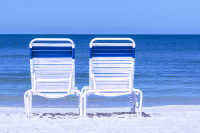Empty chairs on beach against clear sky