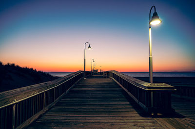 Empty footpath by pier against sky during sunset