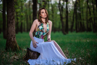 Young woman smiling while sitting on tree trunk in forest