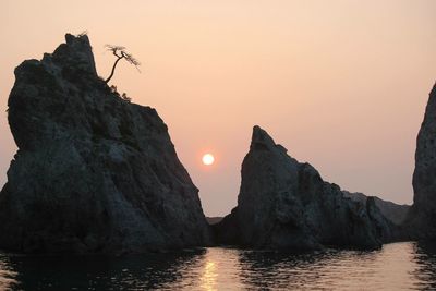 Rock formation in sea against clear sky during sunset