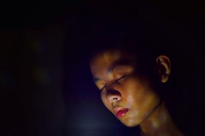 Close-up of young woman with eyes closed against black background