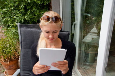 Beautiful young woman using digital tablet outside house