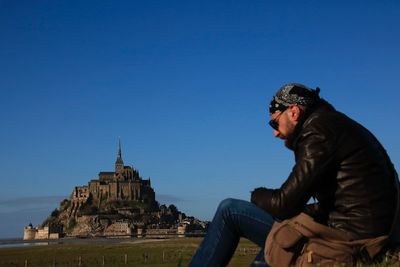 Side view of man sitting at mont saint-michel against clear sky