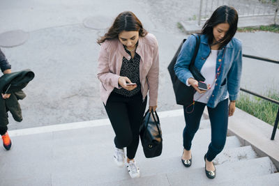 High angle view of female friends moving up on staircase while using smart phones