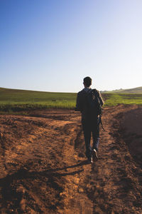 Rear view of man walking on dirt road against clear sky