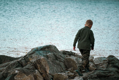 Rear view of boy standing on rock at beach