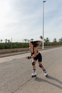 Full body of fit female in activewear with flying hair skating on roller blades and listening to music in tws earbuds