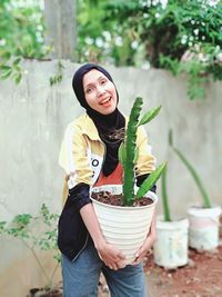 Portrait of smiling woman holding potted plant while standing in yard