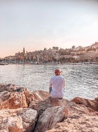 Rear view of man sitting on rock against sky