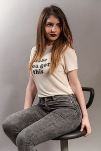 Portrait of beautiful young woman sitting against wall