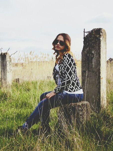 grass, casual clothing, young adult, lifestyles, standing, sitting, person, field, leisure activity, day, built structure, abandoned, three quarter length, plant, outdoors, grassy, architecture, portrait