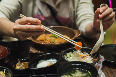 Close-up midsection of woman having meal with chopsticks at table