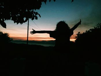 Silhouette woman against trees against sky during sunset