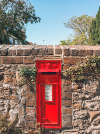 Red mailbox on wall against sky