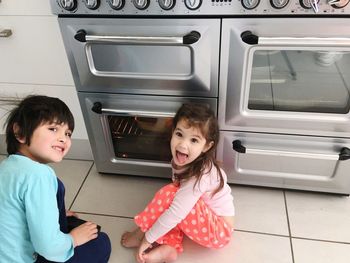 Portrait of siblings by oven on floor in kitchen at home