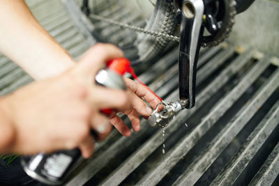 From above of crop anonymous male master using chemical spray and cleaning bike pedal in repair workshop