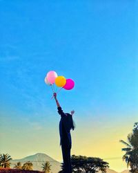 Low angle view of person holding balloons against sky during sunset