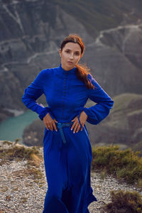 Brunette woman in a blue long dress stands on the edge of the sulak canyon in the evening at sunset