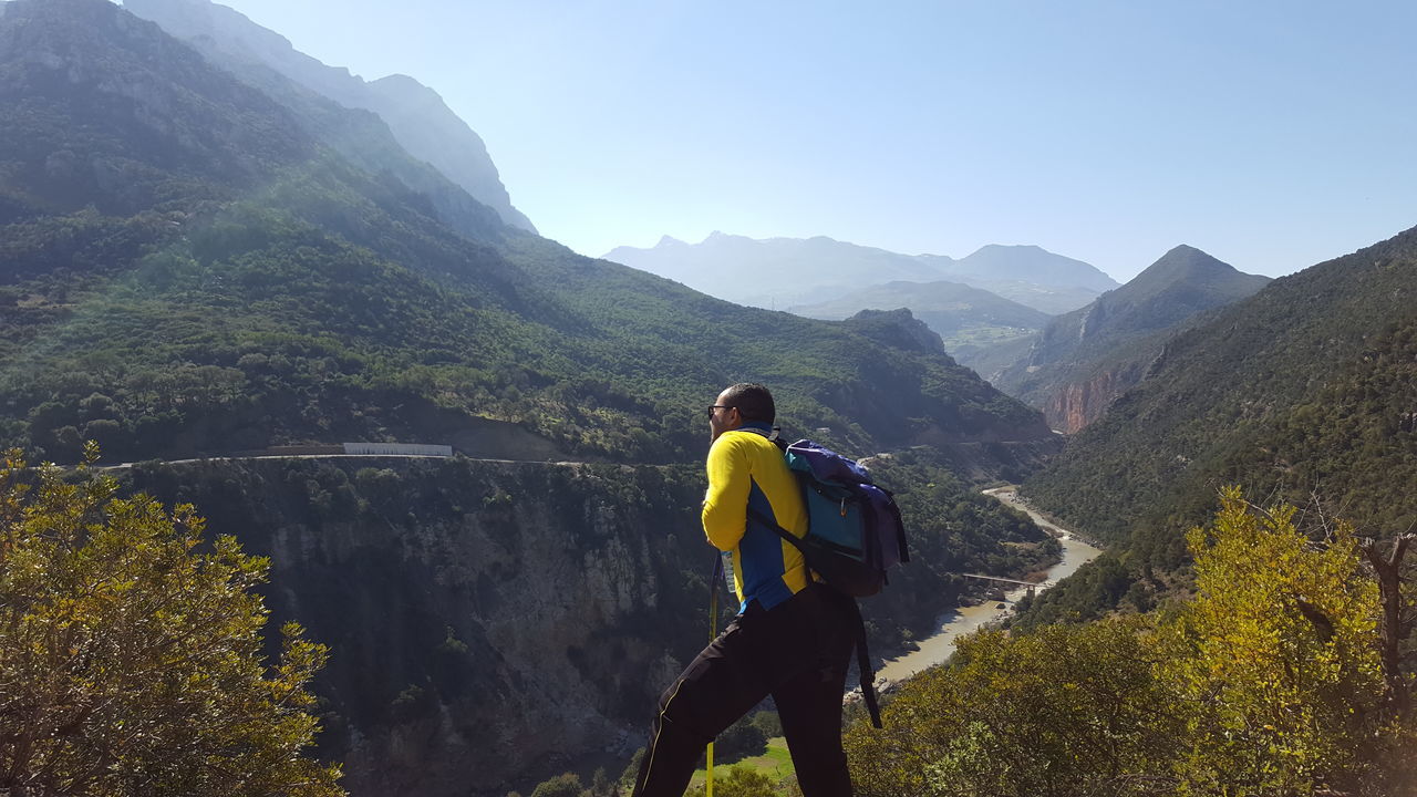 mountain, mountain range, leisure activity, rear view, scenics, lifestyles, full length, beauty in nature, tranquil scene, men, hiking, casual clothing, tranquility, nature, tourist, valley, non-urban scene, adventure, mountain road, tourism, vacations, remote, physical geography, exploration, green color, hiker