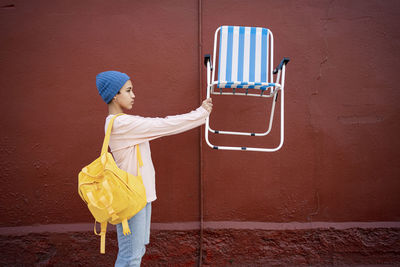 Woman with backpack holding armchair by wall