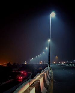 Illuminated street by river against sky at night