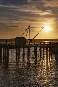 Silhouette bridge over sea against sky during sunset