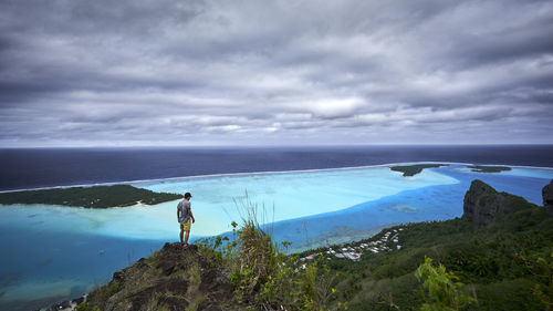 Man standing on rock by sea against sky