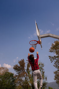 Low angle view of boy playing basketball on court against sky