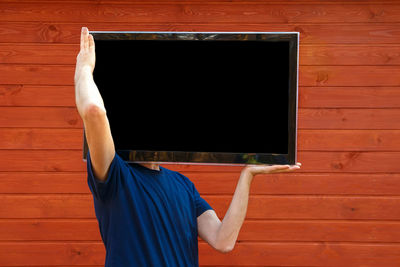 Man carrying television set while standing against wall