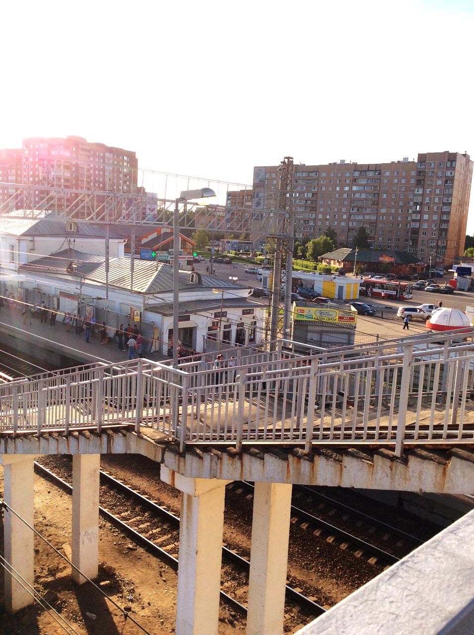 architecture, built structure, building exterior, clear sky, railroad track, city, railing, railroad station, rail transportation, transportation, public transportation, sky, high angle view, city life, railroad station platform, day, outdoors, roof, sunlight, residential building