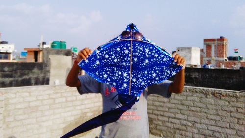 Rear view of woman holding umbrella against blue sky