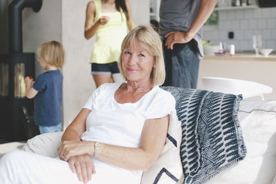 Portrait of smiling senior woman sitting on sofa with family in background