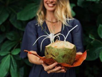 Midsection of smiling young woman holding coconut