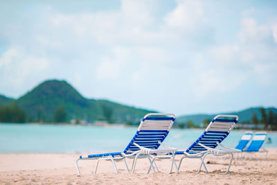 Empty chairs and lounge chair at beach against sky
