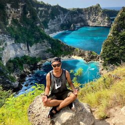 Portrait of young man sitting on rock by sea