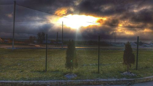 Chainlink fence against cloudy sky at sunset