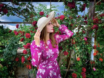 Woman wearing pink dress and sun hat in a garden of roses
