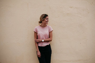 Woman looking away while standing against wall