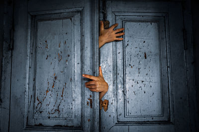 Cropped hands emerging from old gray doors