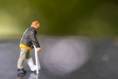 Miniature people , full length view of a man with broken leg is using crutch for walking
