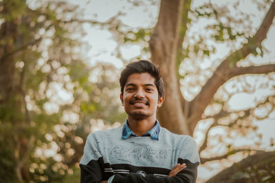 Portrait of young man standing against trees