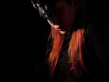 Portrait of redhead woman wearing mask against black background