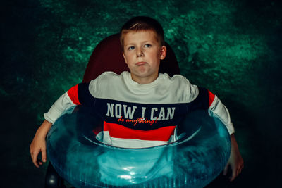 Cute boy with inflatable sitting on seat against wall