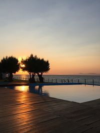 Silhouette trees by swimming pool against sky during sunset