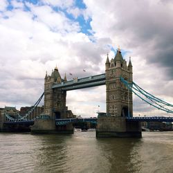 Bridge over thames river against cloudy sky