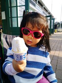 Cute girl wearing sunglasses holding ice cream cone while standing on footpath