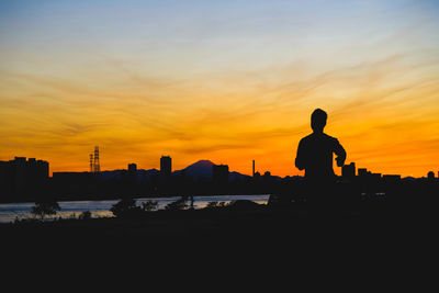 Silhouette man and cityscape against sky during sunset