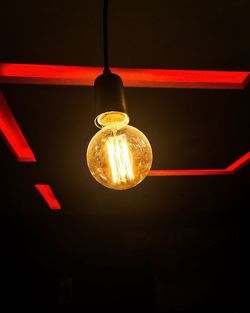 Low angle view of illuminated light bulb hanging in darkroom